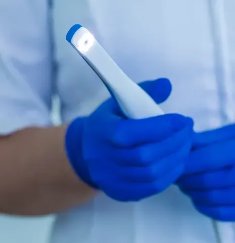 Gloved hands holding a white dental intraoral scanner device