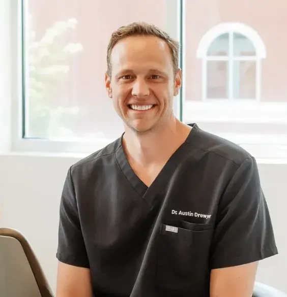 Smiling man in dark gray scrubs labeled "Dr. Austin Drewer" indoors.