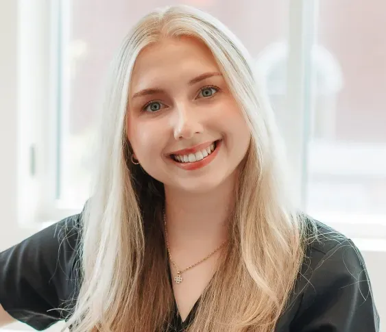 Smiling woman with long blonde hair wearing a black top and gold necklace.